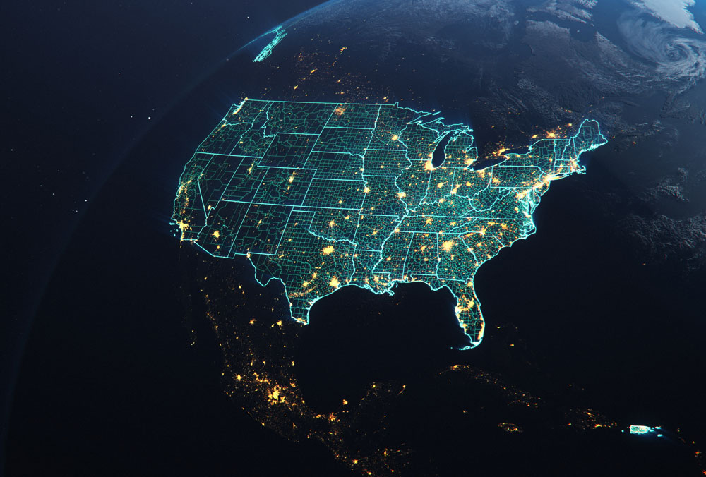 Satellite-style view of the United States at night from space, overlaid with a glowing turquoise digital grid outlining state and county boundaries, with bright clusters of city lights visible across the country and along the coasts.